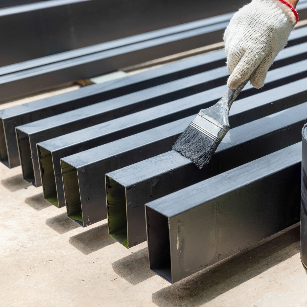 Worker painting steel post in construction site.